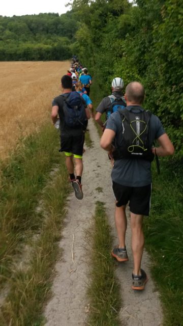 People in front of me running up alongside a field.